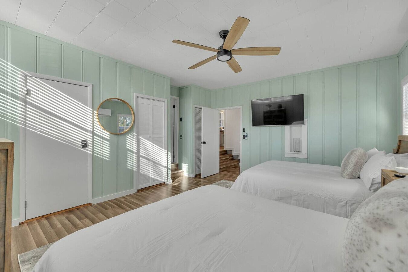 A bedroom with two beds, a ceiling fan, a TV, and a hallway leading to another room.