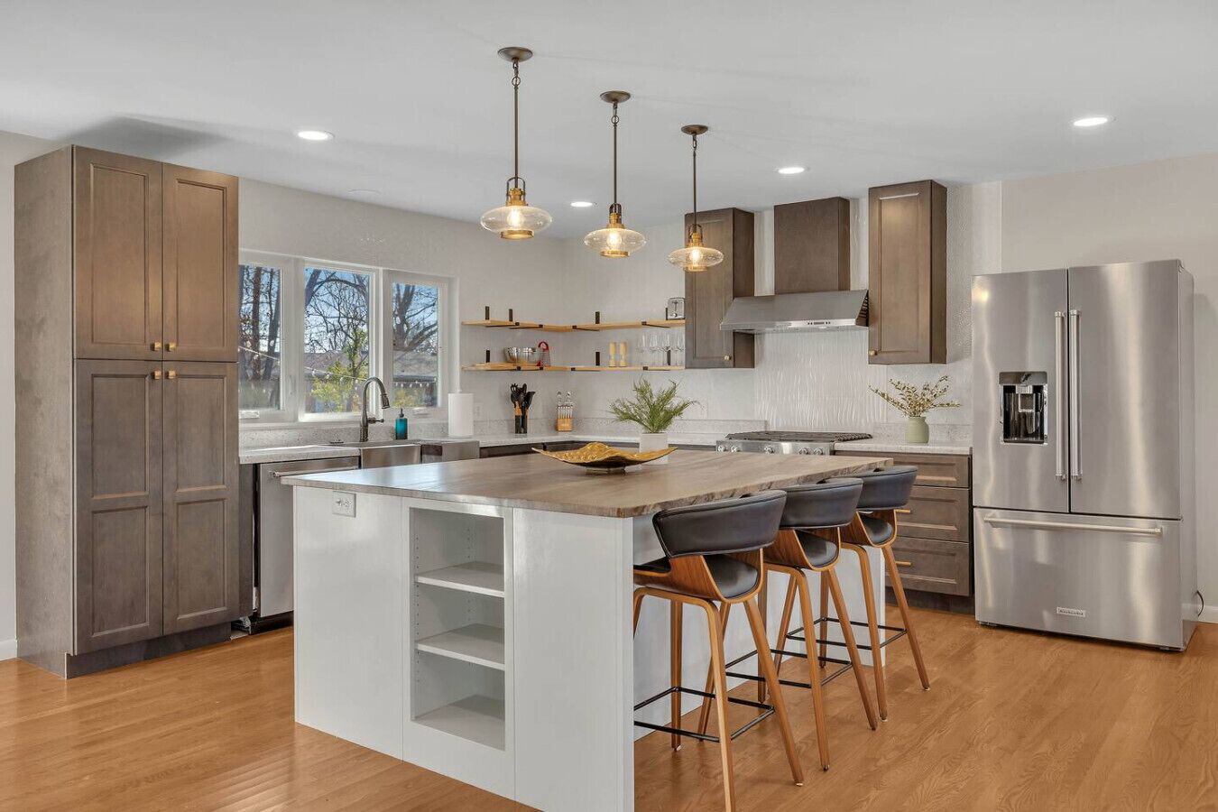 A modern kitchen with a central island, bar stools, stainless steel appliances, and pendant lighting.