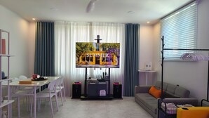 Un salon moderne doté d’un téléviseur à écran plat, d’un ventilateur de plafond, d’un canapé, d’une table à manger avec des chaises et d’un meuble pour téléviseur contenant des appareils électroniques.