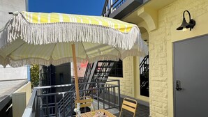 Un balcon avec un parasol à rayures jaunes, une table en bois avec une bouteille et une chaise.
