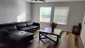 A living room with a black leather sectional sofa, a wooden coffee table, and hardwood flooring.