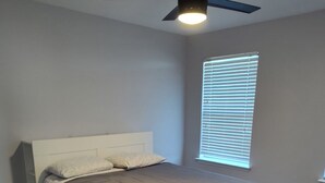 A bedroom with a bed, a ceiling fan, and a window with blinds.