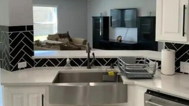 A modern kitchen with white cabinetry, a stainless steel sink, and a ceiling fan.