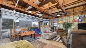 A spacious living area with a foosball table, comfortable seating, and a large window offering a view of the outdoors. - The Lighthouse: Large home close to downtown with a hot tub & game room! (South Haven)