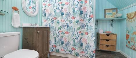 Un baño con inodoro, armario de madera y cortina de ducha estampada con motivos florales.