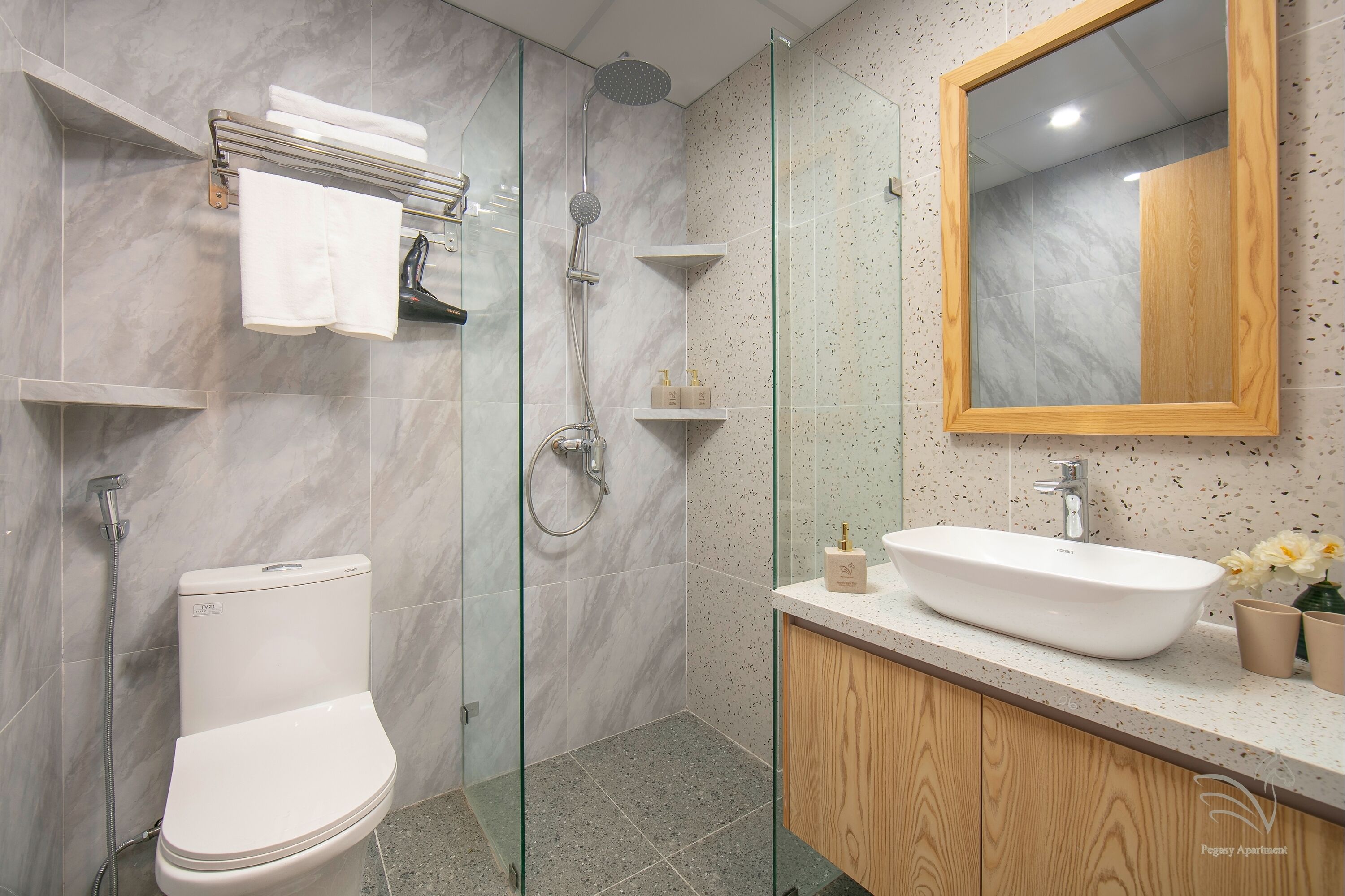Un baño moderno con ducha envuelta en cristal, inodoro blanco y tocador de madera con lavabo.