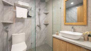 Un baño moderno con ducha envuelta en cristal, inodoro blanco y tocador de madera con lavabo.