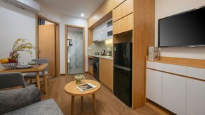 Una cucina compatta con mobili in legno, un forno integrato e un frigorifero nero. In primo piano, un tavolo da pranzo con un vaso di fiori e una rivista.