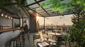 Un caffè all'aperto con un bancone, tavoli e sedie, e vista sullo skyline della città.