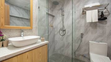Un baño moderno con ducha de vidrio, lavamanos blanco y retrete.