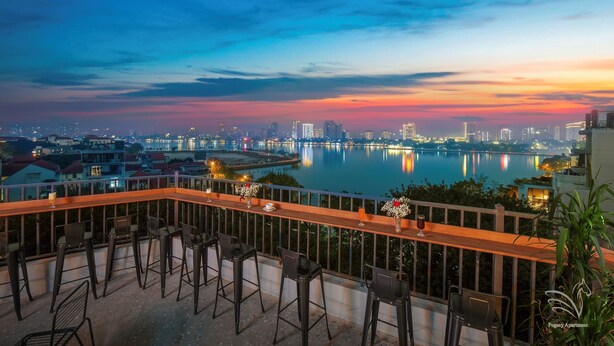 Una terrazza con sedute da bar che si affaccia su una città e un corpo d'acqua al crepuscolo.