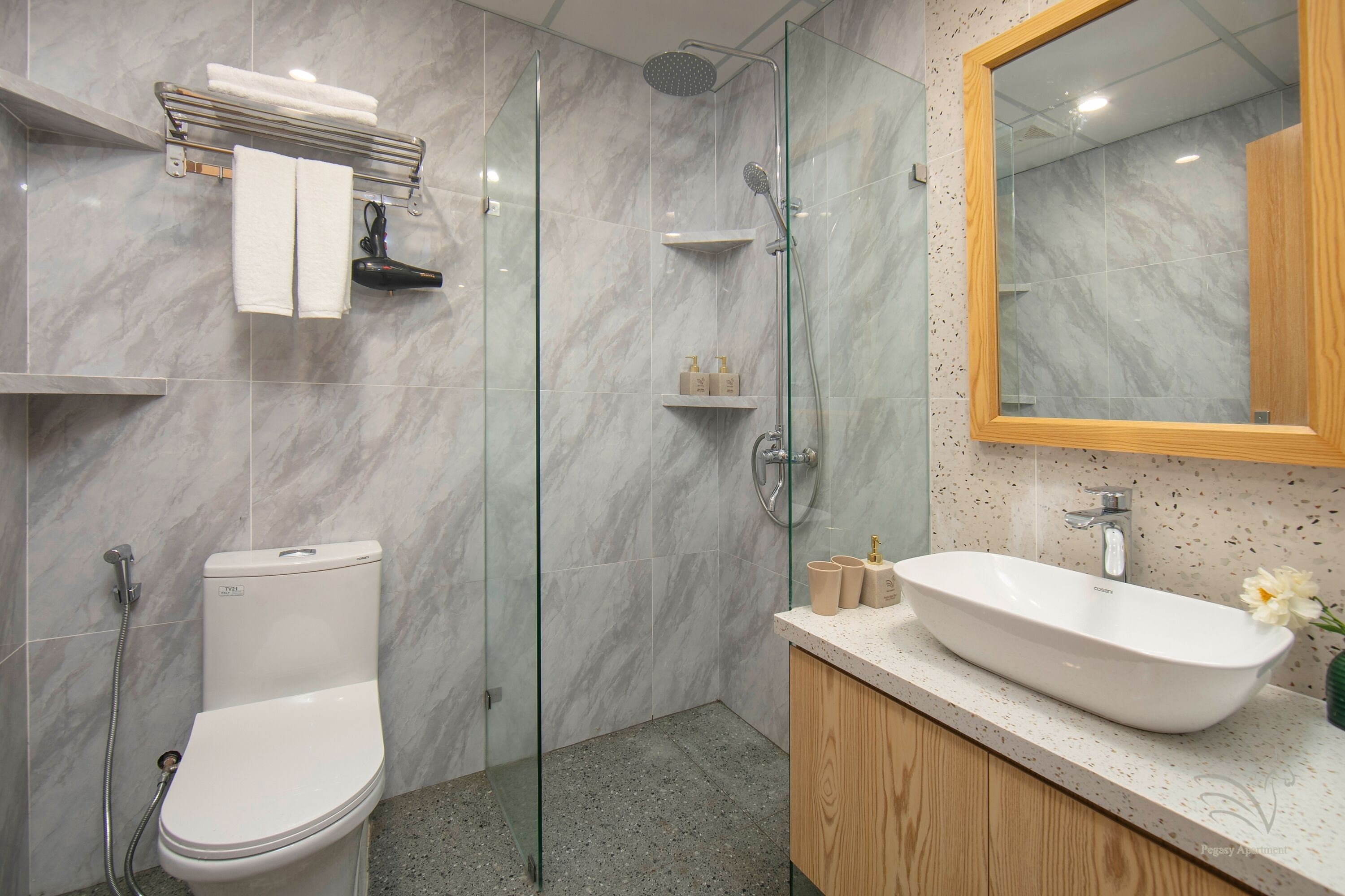A modern bathroom with a glass-enclosed shower, a white toilet, a wooden vanity with a sink, and a marble-tiled wall.