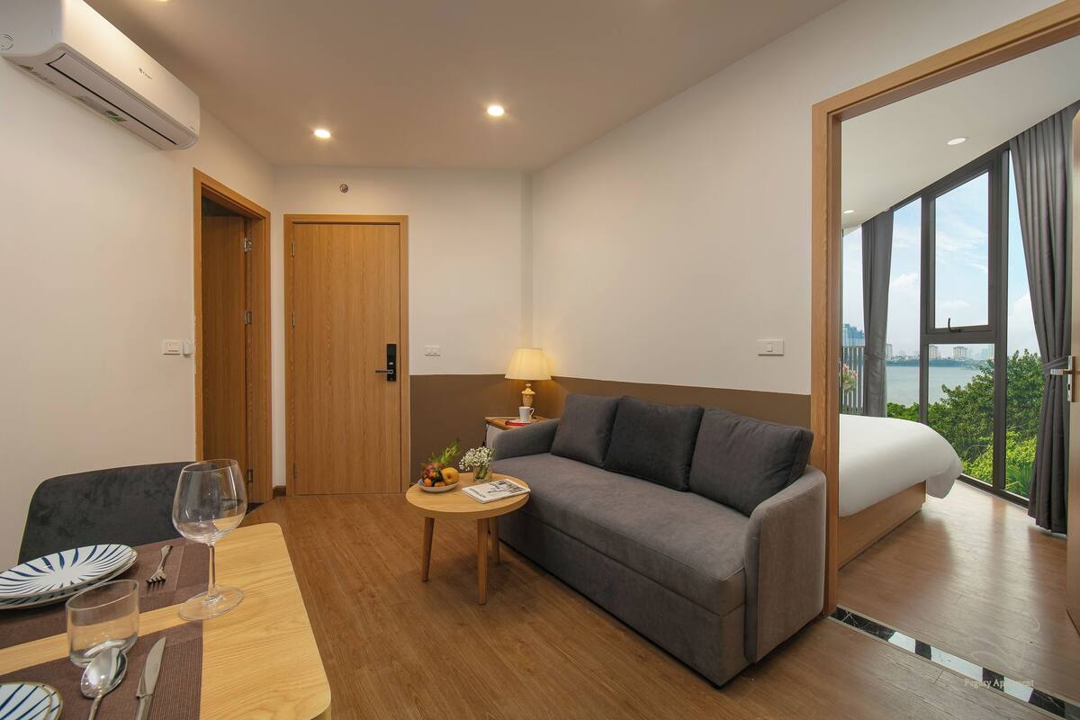 Une chambre d’hôtel moderne, équipée d’un canapé, d’une table à manger avec assiettes et verres, d’une lampe et d’un lit donnant sur la ville.