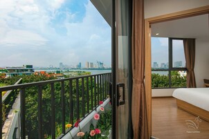 A modern bedroom with a large window, a balcony with flowers, and a city view.