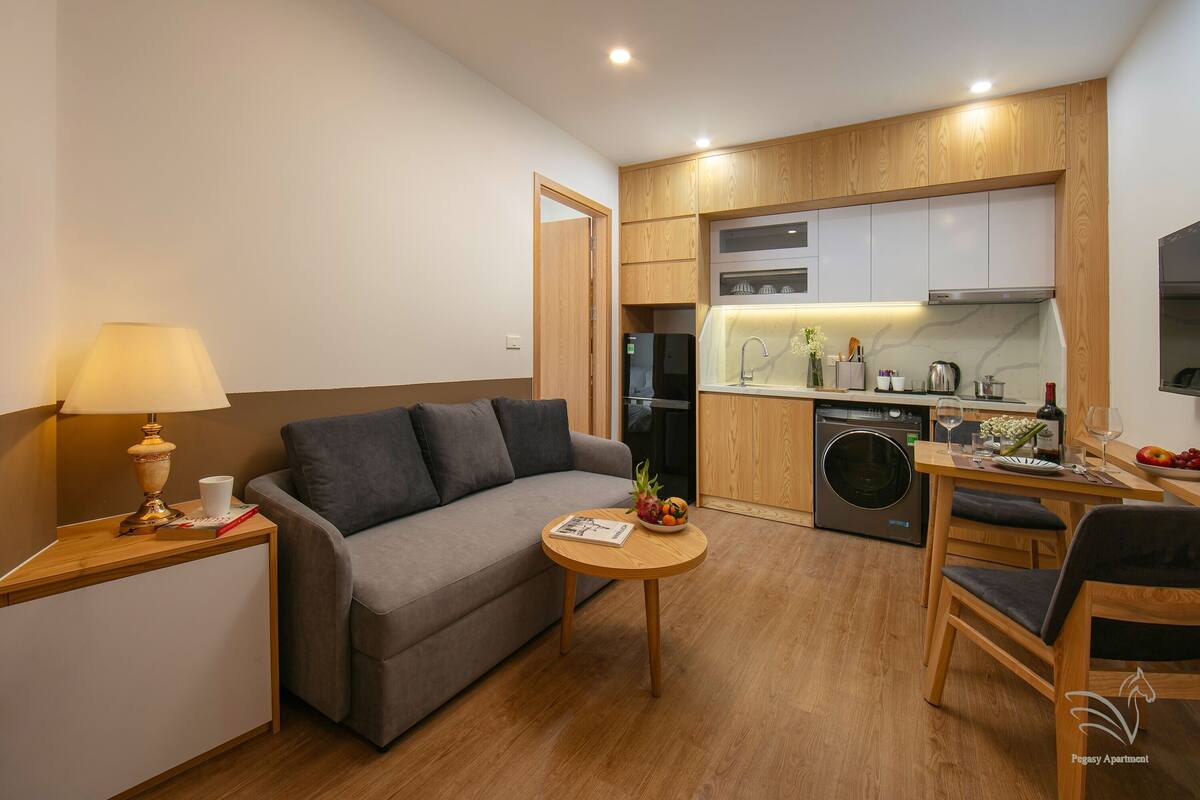 Un espace de vie compact comprenant un canapé, une petite table ronde, une table basse, un coin repas avec une table et des chaises, une cuisine équipée d’un lave-linge et d’un four à micro-ondes.