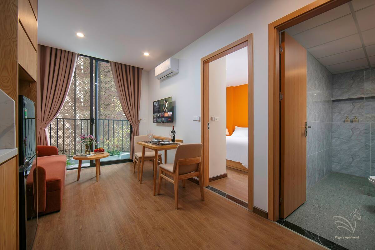 Une chambre d’hôtel moderne avec un plancher en bois, un coin repas comprenant une table et des chaises, une télévision et une grande fenêtre avec des rideaux.