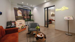 Un centro benessere moderno con area accoglienza, poltrona massaggiante, tavolo con un vaso e una teiera, e insegna luminosa al neon.