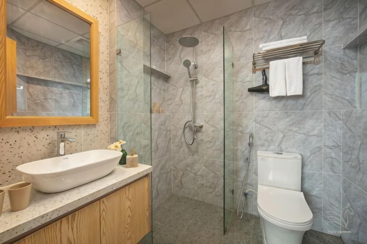 A bathroom with a marble wall, a sink, a toilet, and a shower.