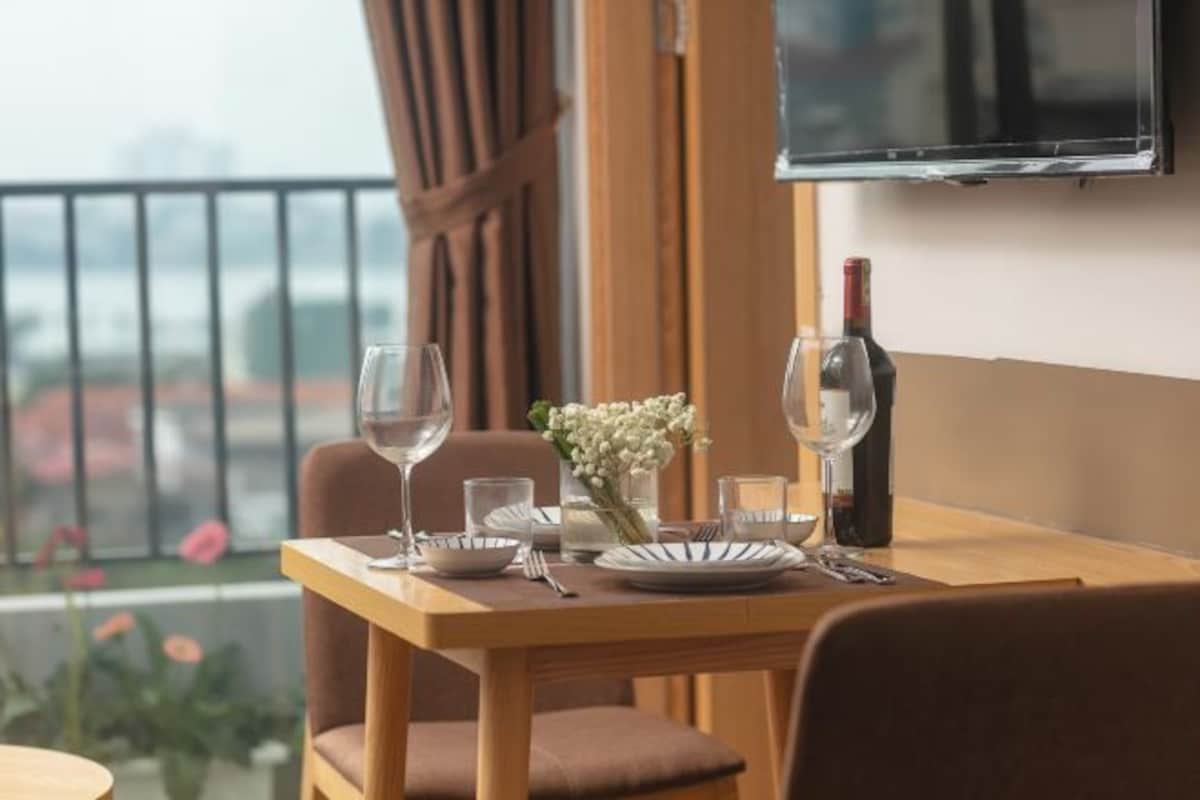 A dining table set with wine glasses, plates, and a bottle, with a city view in the background.