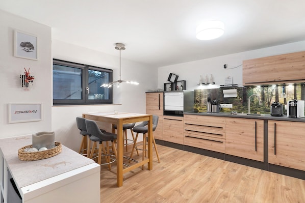 A modern kitchen with wooden cabinets, a dining area with a table and chairs, and a large window.