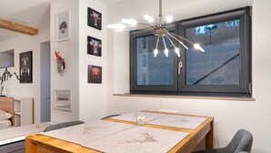 Un coin repas avec une table en bois, des chaises grises, un luminaire au plafond et une fenêtre donnant sur un paysage enneigé.