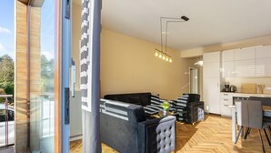 Una sala de estar moderna con un sofá, un comedor con mesa y sillas, una cocina con armarios blancos y un ventanal grande.