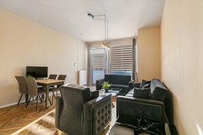 A modern living room with a dining area, a flat-screen TV, and a large window with blinds.
