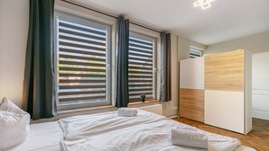 Una habitación de hotel con dos camas, un armario de madera y ventanas amplias con persianas.