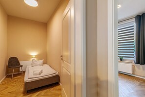 A bedroom with a bed, a chair, a bedside lamp, and a window with blinds.