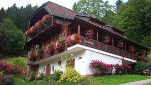 Un chalet traditionnel doté d’un balcon orné de fleurs, d’une façade blanche et d’un jardin luxuriant.