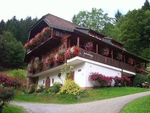 Ein traditionelles Chalet mit Balkon, geschmückt mit Blumen, heller Fassade und üppigem Garten.