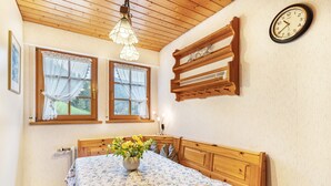 Une chambre avec une tête de lit en bois, un lit recouvert d’une couvre-lit à motifs floraux, une table de chevet ornée d’un vase de fleurs et une horloge fixée au mur.
