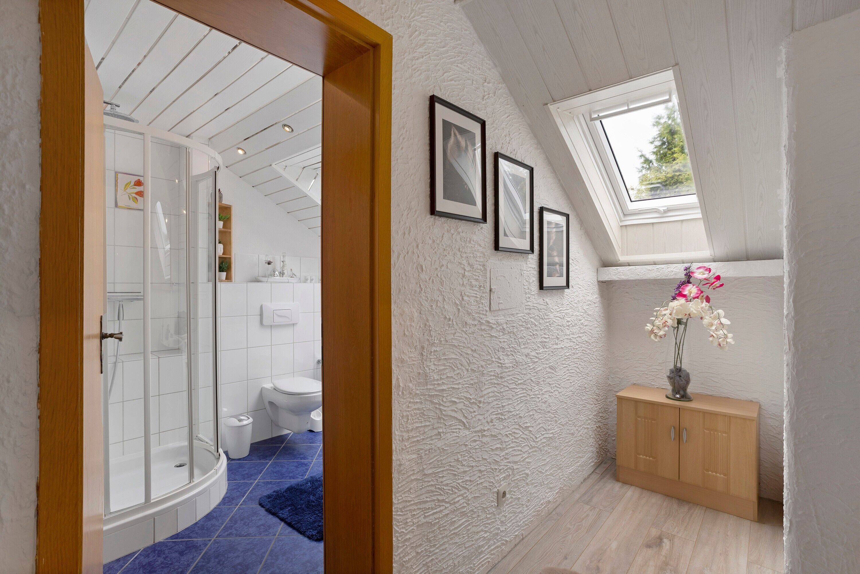 Une salle de bain avec douche, toilettes et lavabo, un meuble en bois et une lucarne.