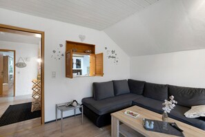 Moderni olohuone, jossa on tummanharmaa sohva, puinen sohvapöytä ja pieni sivupöytä. Seinällä on peili ja lattialla mustavalkoinen matto.