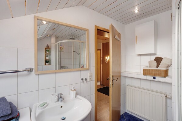 Un baño con un lavamanos blanco, un espejo y una puerta de madera que da a otra habitación.