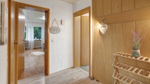 Un pasillo con una puerta de madera, un letrero de bienvenida, una lámpara con forma de corazón y una planta en un estante.
