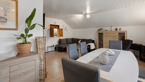 Una sala de estar moderna con comedor, un conjunto de sofá, una planta en maceta y un aparador de madera.