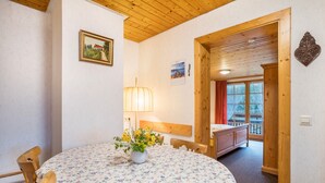 Une pièce avec une table ronde, des chaises en bois, un lit, une fenêtre avec des rideaux et un plafond en bois.