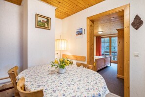 Une pièce avec une table ronde, des chaises en bois, un lit, une fenêtre avec des rideaux et un plafond en bois.