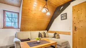 Une pièce chaleureuse avec un plafond en bois, une porte en bois, un canapé, une table basse et une fenêtre avec un rideau.