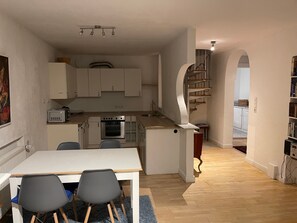 Une cuisine compacte avec un coin repas, un four encastré et un escalier menant à un niveau supérieur.