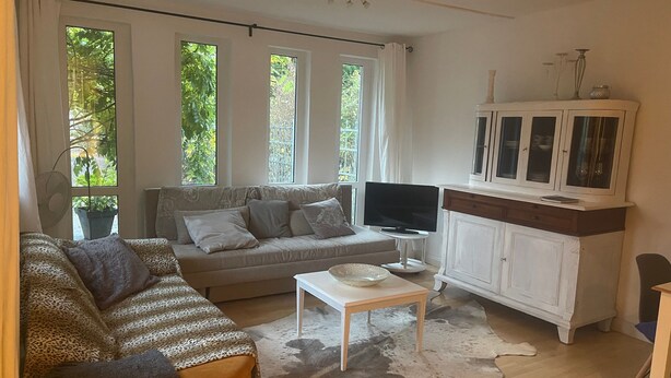Een woonkamer met een bank, een televisie, een kast en een raam met gordijnen.