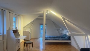 Een slaapkamer in loftstijl met een schuine kap, een bed, een bureau en een stoel.