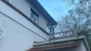 Een wit gebouw met pannendak, een glazen deur, een klein terrasje met een stoel en tafel, en een potplant.