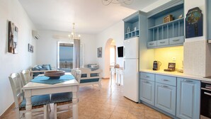 Una cucina con mobili bianchi, un tavolo da pranzo con sedie, un lampadario e una vista attraverso un arco.