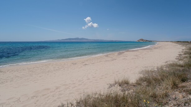 Een strand met heldere lucht, een zandstrand en een berg in de verte.