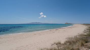 A beach with clear skies, a sandy shore, and a distant mountain.
