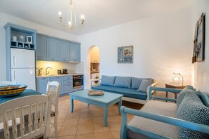 Un espacio habitable compacto con kitchenette, zona de comedor y sala de estar con sofá y sillones.