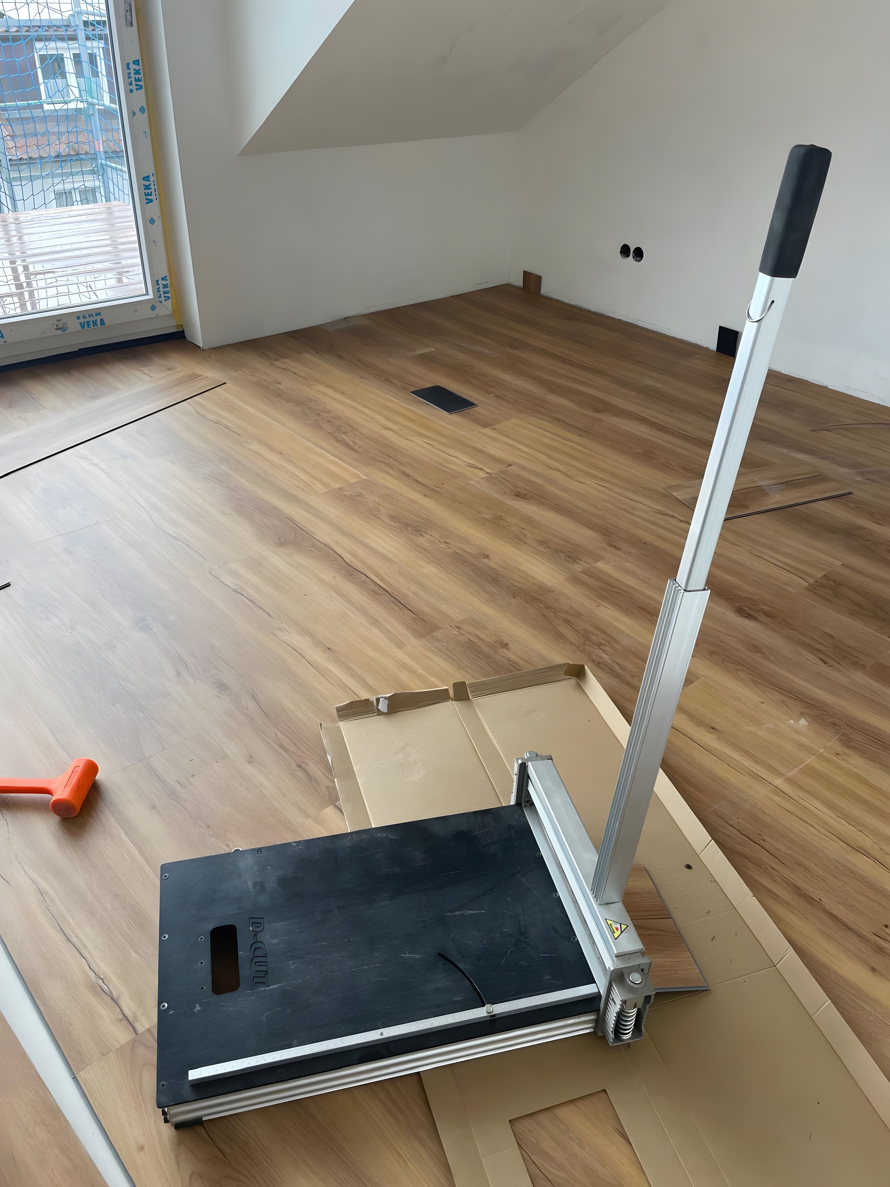 Een kamer met houten vloer, een raam met zonwering en een meubelstuk met een zwart bovenblad.