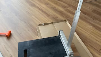 Een kamer met houten vloer, een raam met zonwering en een meubelstuk met een zwart bovenblad.